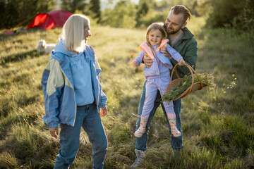 Young caucasian couple with little girl have fun while travel in the mountains. Happy family spending summer vacation at campsite. Father tossing daughter in his arms