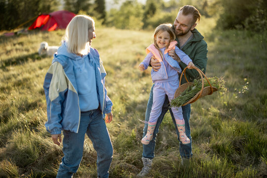 Young caucasian couple with little girl have fun while travel in the mountains. Happy family spending summer vacation at campsite. Father tossing daughter in his arms