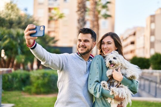 Man and woman holding dog making selfie by the smartphone at park