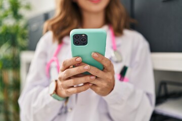 Fototapeta na wymiar Young woman wearing doctor uniform using smartphone at clinic