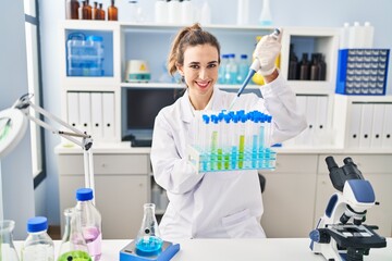 Young woman wearing scientist uniform using pipette working at laboratory