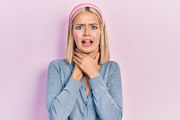 Beautiful blonde woman standing over pink background shouting and suffocate because painful...