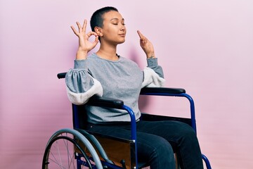 Beautiful hispanic woman with short hair sitting on wheelchair relax and smiling with eyes closed doing meditation gesture with fingers. yoga concept.