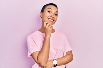 Beautiful hispanic woman with short hair wearing casual pink t shirt looking confident at the camera smiling with crossed arms and hand raised on chin. thinking positive.