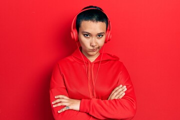 Beautiful hispanic woman with short hair listening to music using headphones skeptic and nervous, disapproving expression on face with crossed arms. negative person.