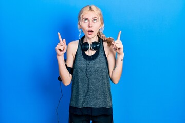 Fototapeta premium Beautiful caucasian woman with blond hair wearing sportswear amazed and surprised looking up and pointing with fingers and raised arms.