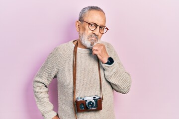 Handsome senior man with beard holding vintage camera thinking concentrated about doubt with finger...