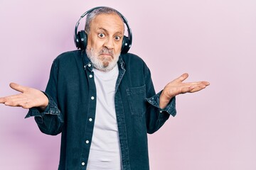 Handsome senior man with beard listening to music using headphones clueless and confused expression...