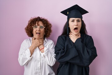 Hispanic mother and daughter wearing graduation cap and ceremony robe shouting and suffocate...
