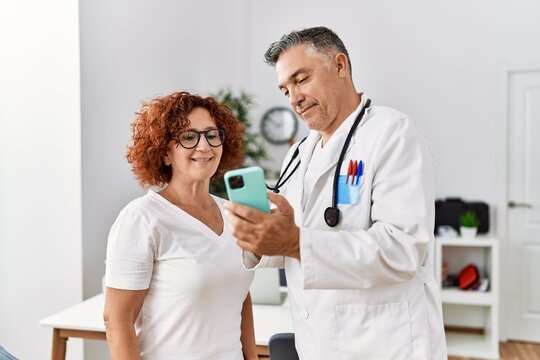 Middle age man and woman wearing doctor uniform using smartphone having medical consultation at clinic