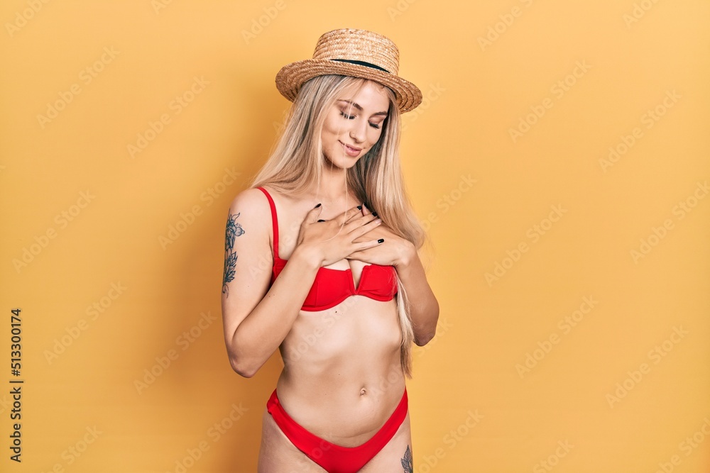 Sticker young caucasian woman wearing bikini and summer hat smiling with hands on chest with closed eyes and