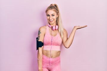 Young beautiful caucasian woman wearing gym clothes and using headphones smiling cheerful presenting and pointing with palm of hand looking at the camera.