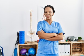 Young african american woman wearing physio therapist uniform standing with arms crossed gesture at...