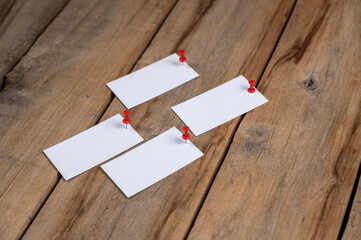 Blank business cards against a wooden background. Four white paper rectangles pinned with push pins...