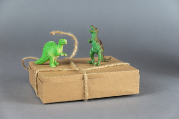 Brown cardboard box and miniatures of two dinosaurs against a gray background. Small green figures...