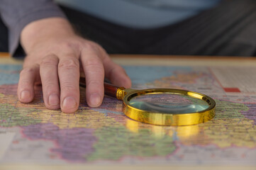 A man holds a magnifying glass in his hand over a map. A middle-aged man with a magnifying glass in a gold frame. The names are written in Ukrainian. Selective focus.