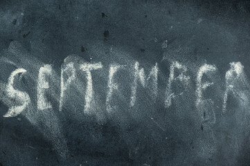 Semi-erased word SEPTEMBER on black chalkboard. Handwritten word. Fuzzy letters on a black surface....