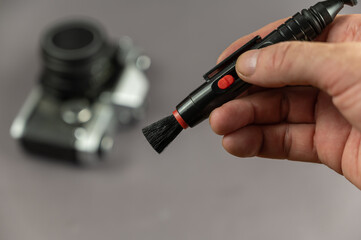 Repair and service of photographic equipment concept. A middle-aged man holding a special brush in his hand. Special brush for cleaning. Vintage camera in the background. Selective focus. Indoor.