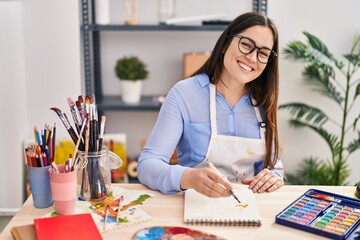 Young woman artist smiling confident drawing on notebook at art studio