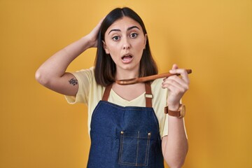 Hispanic girl eating healthy  wooden spoon crazy and scared with hands on head, afraid and surprised of shock with open mouth