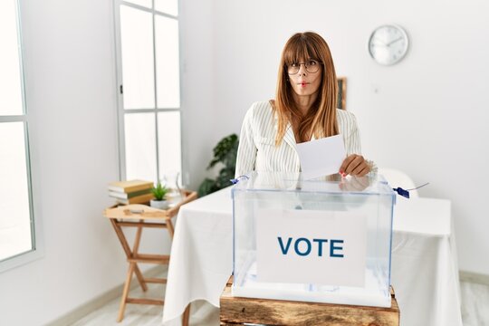 Hispanic business woman voting putting envelop in ballot box making fish face with lips, crazy and comical gesture. funny expression.