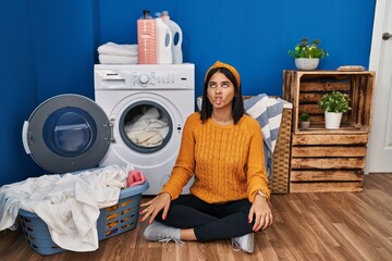 Young hispanic woman doing laundry making fish face with lips, crazy and comical gesture. funny expression.