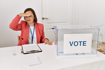 Beautiful middle age hispanic woman at political election sitting by ballot covering eyes with hand, looking serious and sad. sightless, hiding and rejection concept