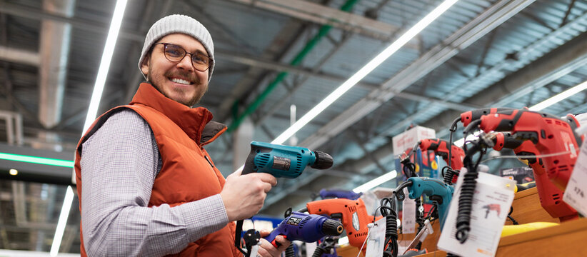 happy customer chooses screwdriver and drill in household goods store