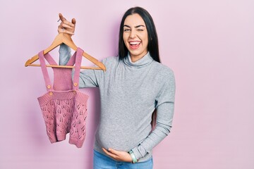 Beautiful woman with blue eyes expecting a baby holding baby clothes winking looking at the camera...