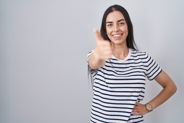 Obraz premium Young brunette woman wearing striped t shirt smiling friendly offering handshake as greeting and welcoming. successful business.