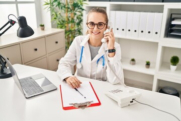 Young doctor woman speaking on the phone looking positive and happy standing and smiling with a confident smile showing teeth