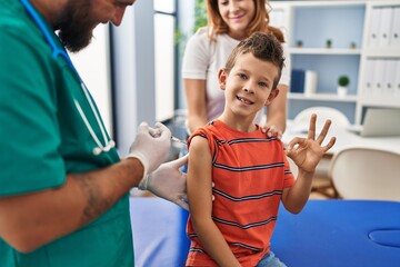 Young kid getting vaccine at doctor clinic doing ok sign with fingers, smiling friendly gesturing...