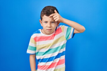 Young caucasian kid standing over blue background pointing unhappy to pimple on forehead, ugly...