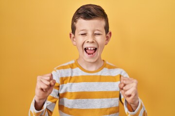 Young caucasian kid standing over yellow background excited for success with arms raised and eyes...