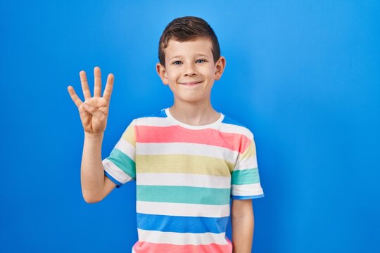 Young caucasian kid standing over blue background showing and pointing up with fingers number four while smiling confident and happy.