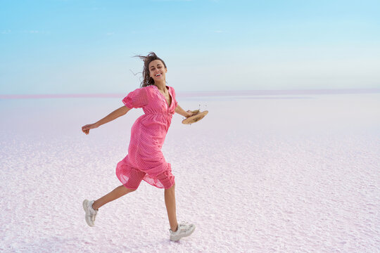 Motion image of happy woman in pink dress running by desert beach of pink lake salt flats.