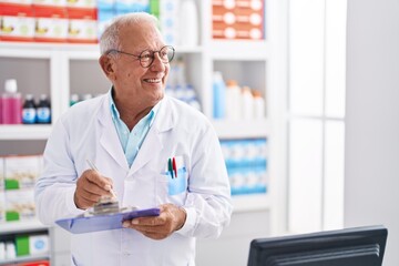 Naklejka na ściany i meble Senior grey-haired man pharmacist writing on document at pharmacy