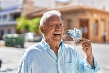 Senior grey-haired man smiling confident holding dollars at street