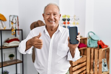 Senior man holding smartphone at retail shop smiling happy pointing with hand and finger to the side