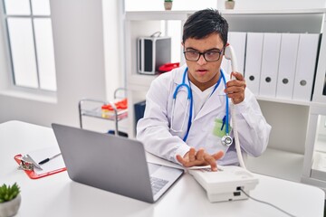 Obraz premium Down syndrome man wearing doctor uniform talking on the telephone at clinic
