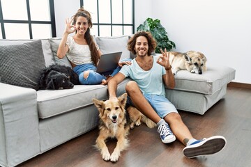 Young hispanic couple with dogs relaxing at home smiling positive doing ok sign with hand and fingers. successful expression.