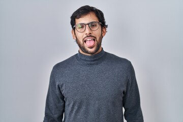 Fototapeta premium Handsome latin man standing over isolated background sticking tongue out happy with funny expression. emotion concept.