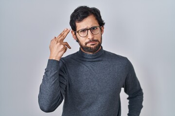 Handsome latin man standing over isolated background shooting and killing oneself pointing hand and...