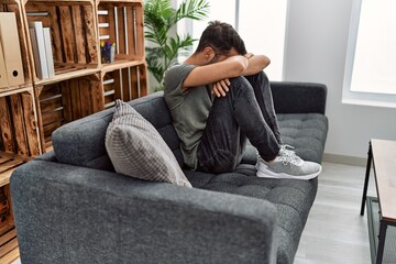 Young hispanic man psychology patient depressed sitting on sofa at clinic