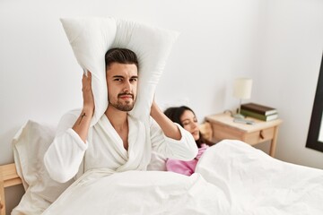 Man covering ears with pillow irritated for snore lying in bed at home.