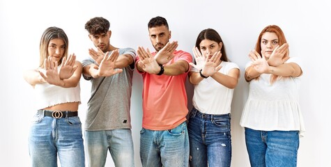 Group of young friends standing together over isolated background rejection expression crossing arms and palms doing negative sign, angry face