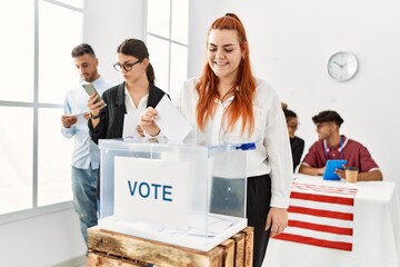 Young american voter woman smiling happy putting ballot in voting box at vote center