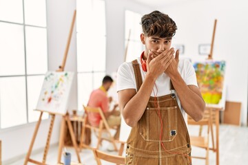 Young hispanic man at art studio shocked covering mouth with hands for mistake. secret concept.