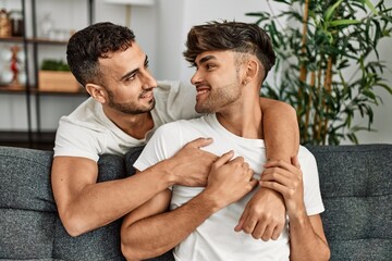 Two hispanic men couple smiling confident and hugging each other at home