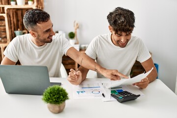 Two hispanic men couple smiling confident using laptop working at home